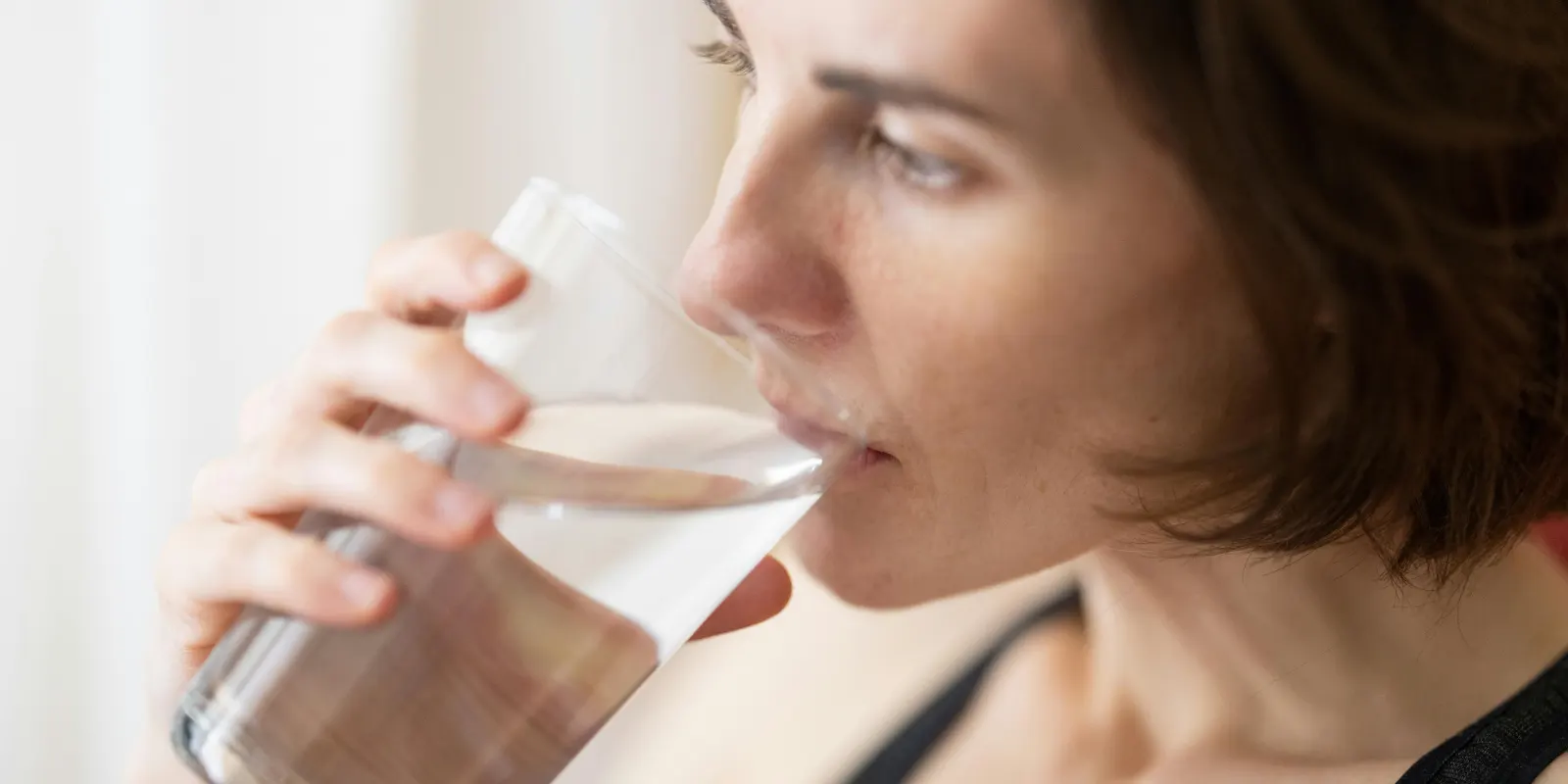 Vrouw geniet van een glas water dat behandeld is met een waterontharder, voorkomt kalkaanslag zonder de natuurlijke mineralen te verwijderen